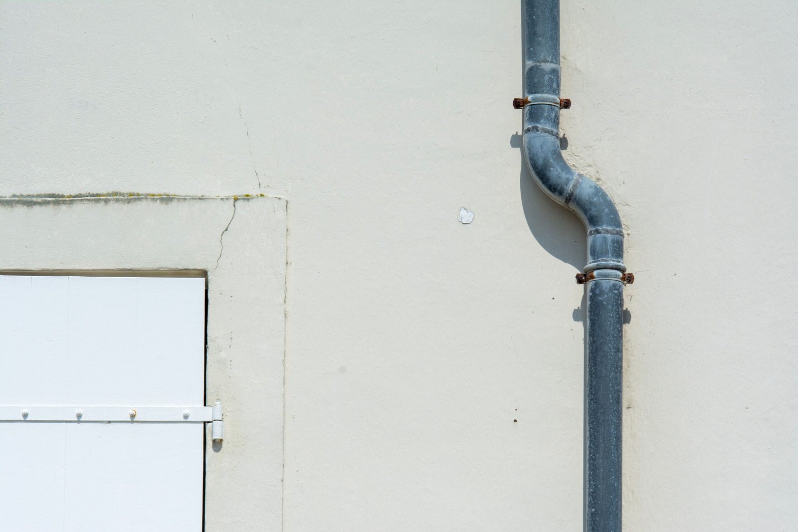 Close-up of a gray metal drainpipe attached to a plain exterior wall.